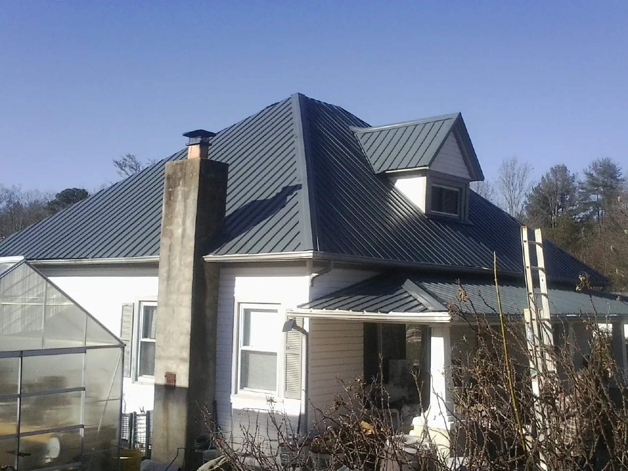 Dark blue standing seam metal roof on a white farmhouse with dormer — Slate & Tile Roof Repair by Roofing Brothers in Baldwin City