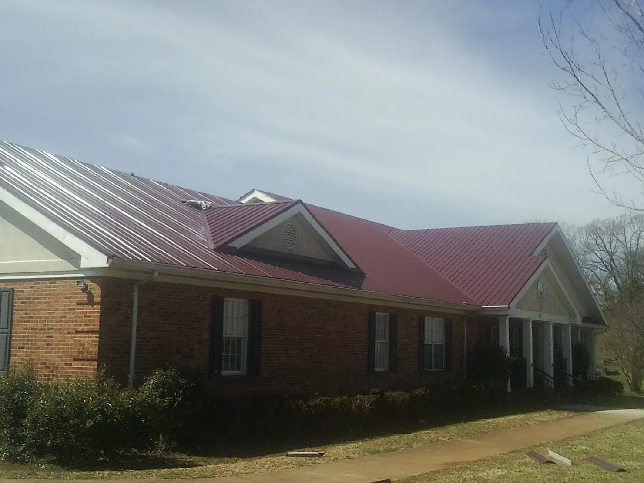Red metal roof with gabled entries on a long brick building, from a Hail Damage Roof Repair job in Baldwin City