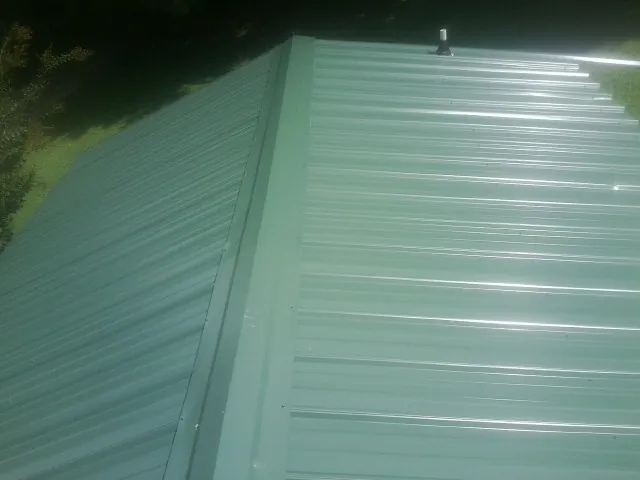 New green metal panels meeting at the ridge of a roof — Flat Roof Repair work by our crew in Baldwin City