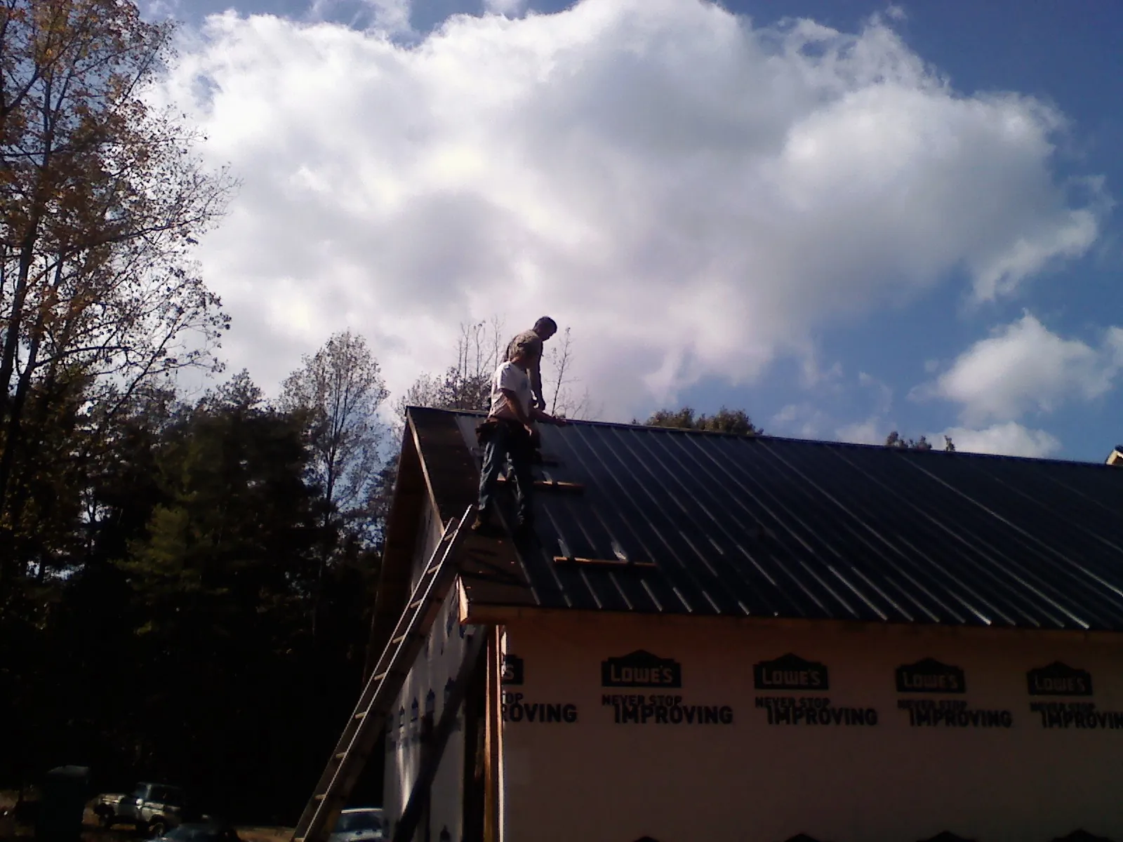 Roofer fastening dark metal panels high against a cloudy sky, from a Roof Inspection job in Baldwin City