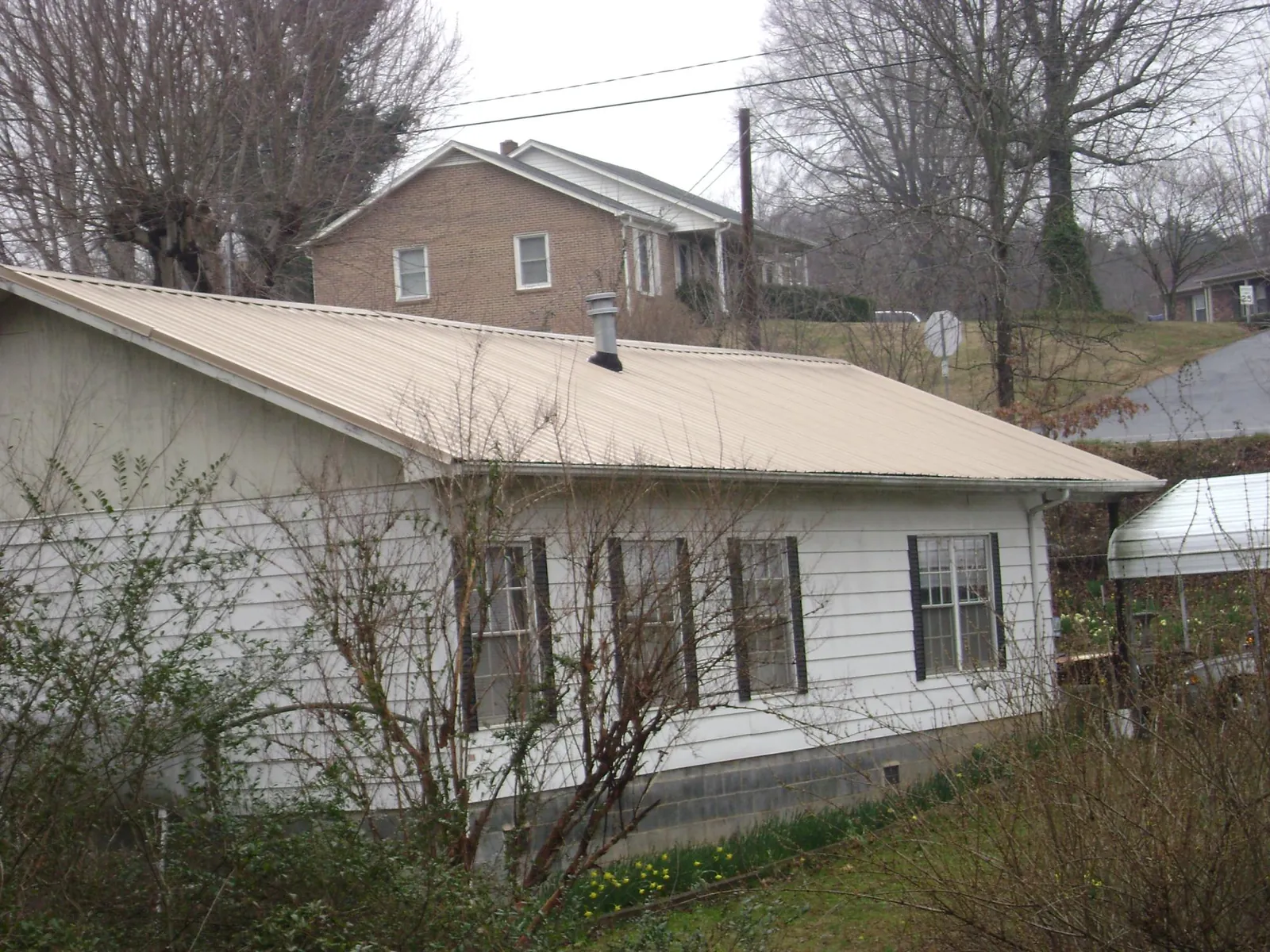 Tan metal roof on a white sided house set into a hillside — Commercial Roofing by Roofing Brothers in Baldwin City
